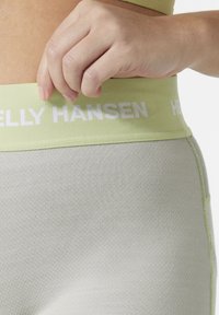 Cintura atlética verde claro con la marca blanca "HELly HANSEN", combinada con una tela gris texturizada. Primer plano de una mano ajustando la cintura.
