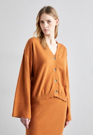 V-hals, oversized cardigan i oransje ullblanding. Har ribbestrikket kant og seks store sølvknapper foran. Mykt, teksturert stoff.