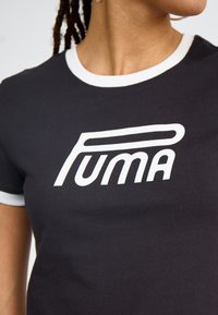 Tricou negru cu inscripția albă "PUMA" într-un font îndrăzneț și modern. Are un guler rotund cu margine albă și o textură netedă din bumbac.