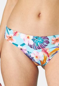 Parte inferiore di bikini floreale con una base blu chiaro decorata da ibischi rosa e viola e foglie tropicali. Il tessuto appare morbido con una fascia elastica in vita.
