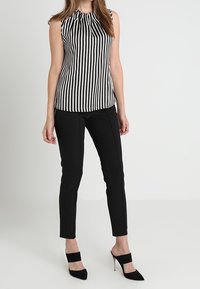 Haut sans manches à rayures noires et blanches avec un col froncé, associé à un pantalon noir ajusté et des chaussures à talons hauts noires.