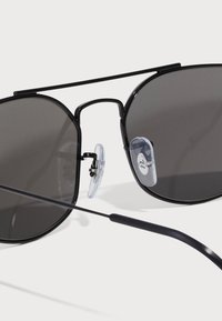 Ochelari de soare aviator negri cu lentile întunecate, ramă subțire din metal negru și tampoane pentru nas transparente. Prezintă un design elegant, minimalist pentru un aspect modern.