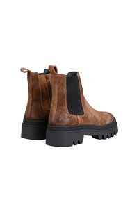 Brown suede Chelsea boots with black elastic side panels, pull tab, and chunky black rubber soles featuring deep treads for grip.
