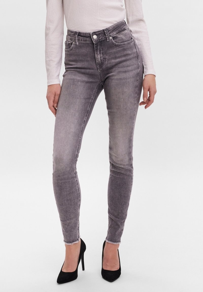 Szare wąskie dżinsy z wysokim stanem, z wybledzonym teksturem i surowym wykończeniem, połączone z czarnymi szpilkami. Materiał z denimu bawełnianego.