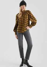 Geel en zwart geblokte blouse met pofmouwen, gecombineerd met donkere grijze jeans en zwarte enkellaarsjes met hak.