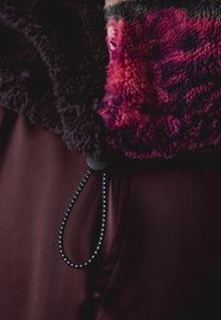 Kurtka polarowa o ciemnofioletowej puszystej fakturze z różowymi i zielonymi akcentami, zapinana na guziki, z czarnym sznurkiem do regulacji.