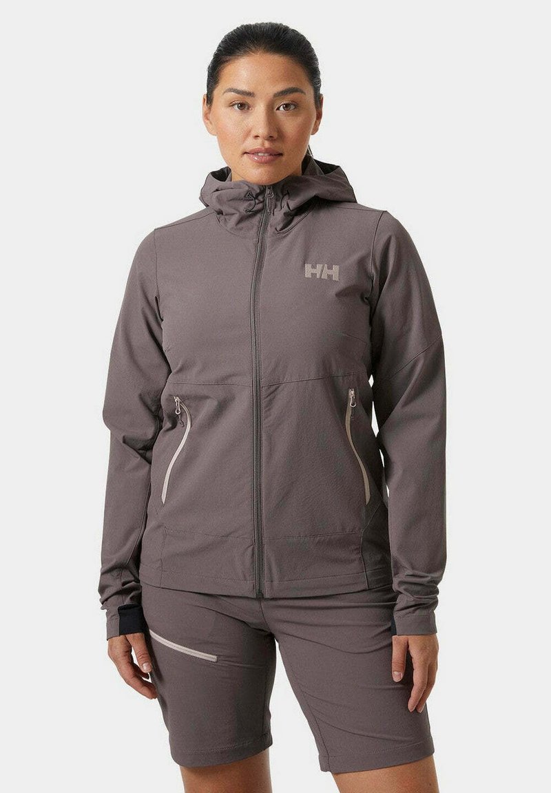 Chaqueta ligera gris con capucha, bolsillos con cremallera y un logo. Presenta una textura suave y un diseño entallado, combinada con pantalones cortos a juego.