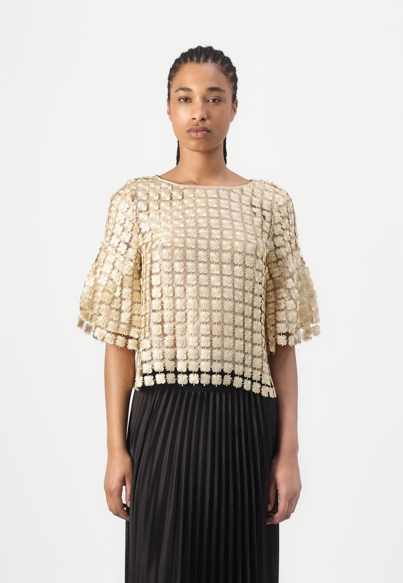 Top à manches courtes avec un motif floral texturé en or métallique. Encolure arrondie et design de manches ouvertes, associé à une jupe plissée noire.