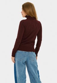 Burgundy garbó pulóver bordás részletekkel, világoskék, széles lábú farmernadrággal kombinálva, hátzsebekkel és kopott részlettel.