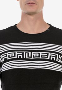 Schwarzer Pullover mit horizontalen weißen Streifen und grafischem Textmuster. Verfügt über einen gerippten Rundhalsausschnitt und eine weiche Textur.