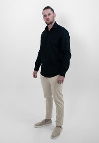 Zwarte, langemouwen knoopshirt, beige slim-fit broek en beige instapschoenen. Eenvoudig ontwerp zonder zichtbare patronen of hardware.