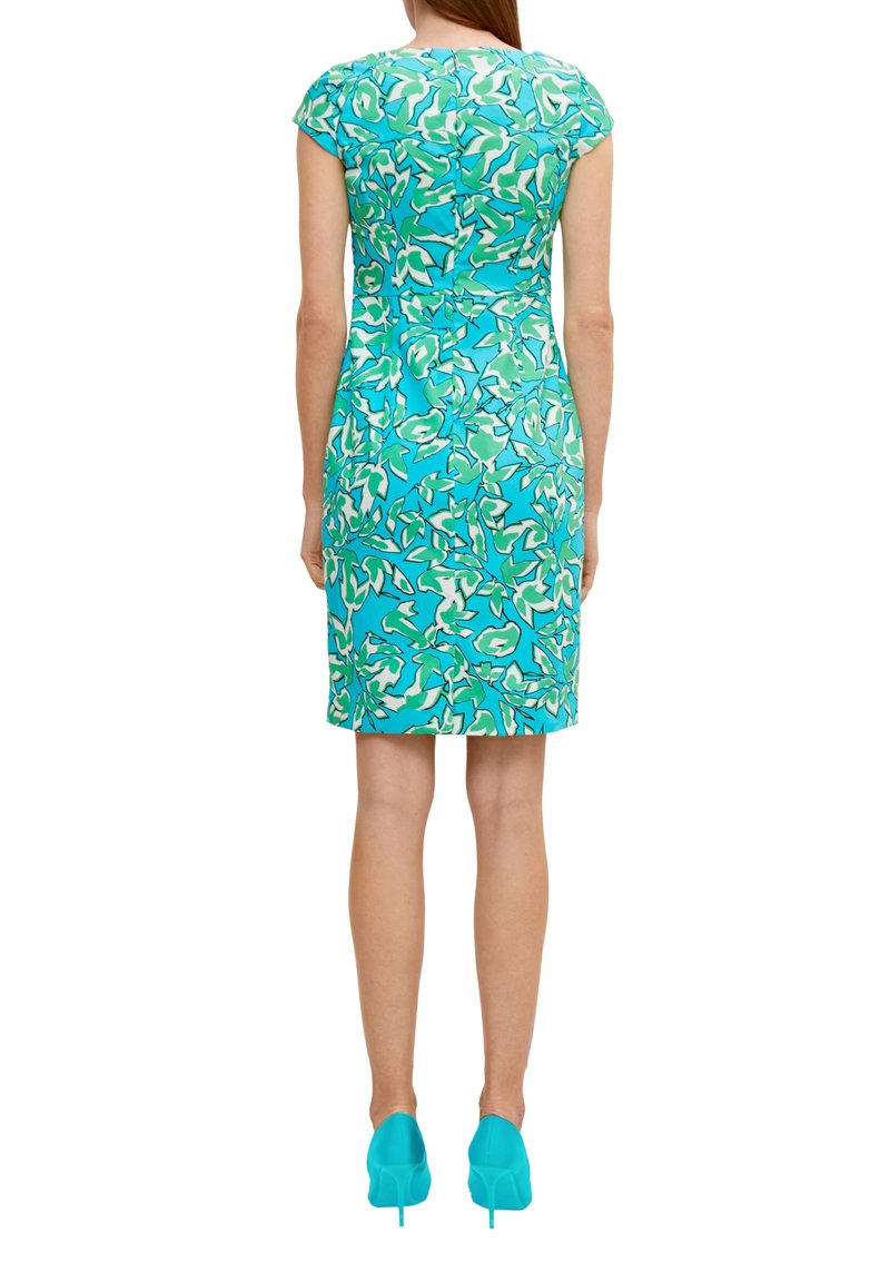 Ärmelloses Kleid in Teal mit einem floralen Muster in Grün und Weiß. Figurbetonte Silhouette mit knielangem Saum und passenden tealfarbenen High Heels.