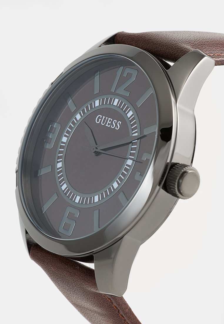 Reloj de pulsera para hombre de Guess con esfera negra, marcadores plateados, tres manecillas que marcan las 2:14 y correa de cuero marrón.