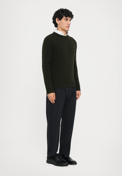 Pull en maille vert foncé avec un col rond, des poignets et un ourlet côtelés, associé à un pantalon noir et des chaussures noires. Design simple et texturé.