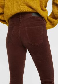 Person wearing dark brown corduroy pants and a mustard yellow knitted sweater, shown from the back at waist level.