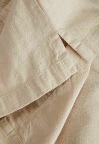 Tissu en lin beige clair avec coutures visibles et une petite fente, montrant la texture et les plis naturels.