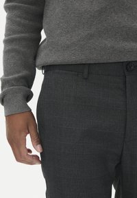 Siv sweater iz pletenine z teksturiranim zaključkom, v kombinaciji s temno sivo karirastimi hlačami, ki imajo subtilen moder mrežni vzorec in zapenjanje na gumb.