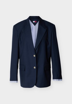 Marineblå enkeltbreasted blazer med to sølvknapper, hakkede revers, klaplommer og stribede skjortearme synlige ved ærmerne.