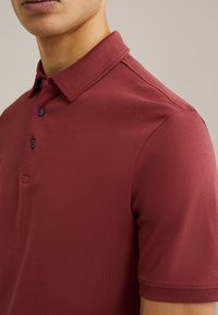 Camisa polo burdeos con cuello clásico, dos botones y mangas cortas. Fabricada con una tela suave y con una textura sutil.