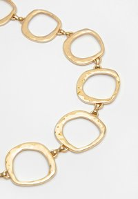 Guldfarvet kædedesign med en række polerede, uregelmæssige kvadratiske led, der er forbundet med små spænder, og som viser en struktureret overflade.