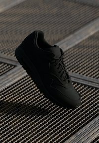 Svart atletisk sneakers med glatt skinnøvre, rund tå og teksturert gummisåle med snøring. Ingen synlige logoer eller mønstre.