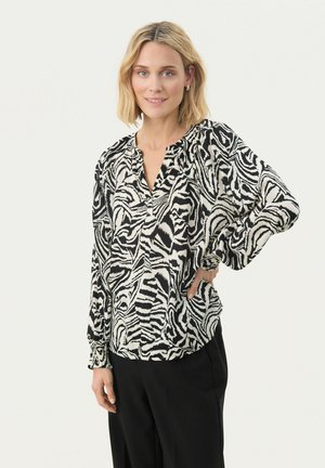 Sort og hvid zebra mønster bluse med v-hals, samlet ærmer og løs pasform, lavet af letvægtigt stof. Sammen med sorte bukser.