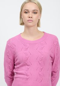 Maglione rosa a maglia con un motivo testurizzato e collo a costine. Maniche lunghe con ritagli intricati in tutto il tessuto.