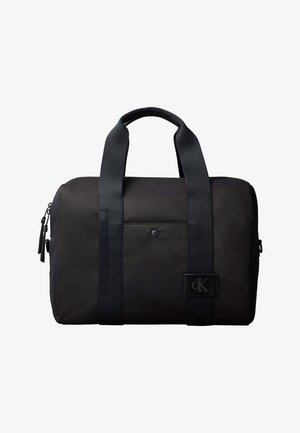 Schwarze rechteckige Reisetasche mit zwei Griffen, vorderer Tasche mit Druckknopf, seitlichen Reißverschlüssen und kleinem Calvin Klein Logo-Patch.