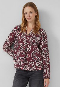 Langärmlige Bluse in einem tiefen Burgunderrot mit einem floralen Paisleymuster in Weiß, Rot und Blau. Mit V-Ausschnitt und gerafften Bündchen.