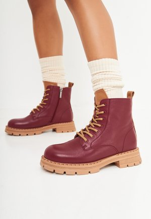Bottines en cuir bordeaux avec des accents beige, à lacets à l'avant, fermeture éclair sur le côté, semelle texturée et plateforme en caoutchouc épaisse.