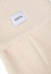 Blødt fleece stof i cremfarge med et label med brandnavnet "CECIL." Tekstureringens overflade har et luksuriøst, varmt udseende.