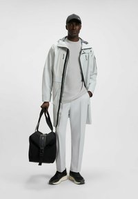 Lightweight, water-resistant jacket in white with black accents, paired with a gray shirt and white pants. Holds a black bag with a zipper.