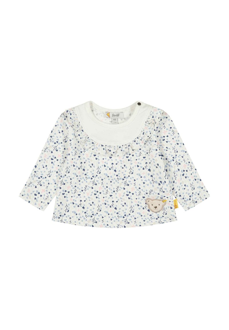 Top a maniche lunghe di colore crema con stampa floreale in blu e rosa. Presenta un colletto arricciato e una toppa di un orso ricamata sul davanti.