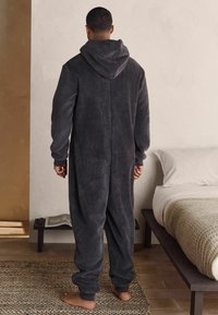 Salopetă din polar gri cărbune, cu glugă, mâneci lungi și manșete elastice. Textură moale și croială lejeră. Design simplu, fără modele vizibile.
