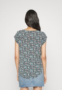 Blouse fleurie à manches courtes, avec un motif bleu, marron et blanc, un ourlet arrondi, et un zip au dos.