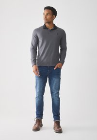 Gray long-sleeve polo shirt with a black collar, paired with blue denim jeans and brown leather boots. Simple, fitted design.