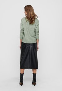 Pull en tricot vert à manches longues, associé à une jupe midi en cuir noir et des bottines à talons châtaigne. Design simple et épuré.