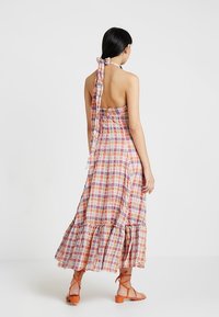 Maxiklänning med rutigt mönster i rosa, orange och vitt, med halterneck och volangkant. Tillverkad av lätt tyg.