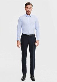 Jasnoniebieska koszula z długim rękawem, z guzikami; granatowe spodnie; czarny pasek; czarne buty wizytowe. Czysty design, dopasowany krój, bez widocznych wzorów.