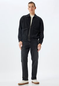 Mustanharmaa farkkutakki, joka on varustettu vetoketjulla, kahdella etutaskulla ja joustavilla hihansuilla, yhdistettynä samanvärisiin mustiin farkkuihin ja vaaleanbeigeihin lenkkareihin.