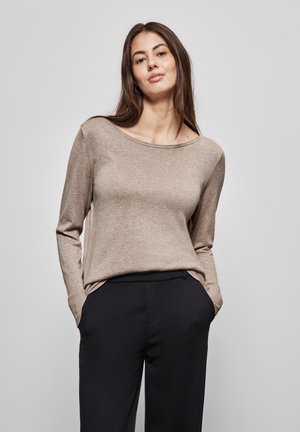 Pull en tricot beige à manches longues avec un col large. Le tissu semble doux, associé à un pantalon sombre, créant une silhouette décontractée.