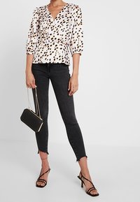 Vit blus med brunt leopardmönster, v-ringning och puffärmar, i kombination med svarta skinny jeans och svarta klacksandaler med remmar. Svart handväska.