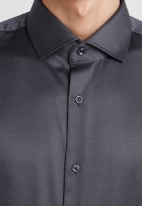 Camicia button-up grigia scura con un motivo a righe sottili, colletto strutturato e bottoni arrotondati nella parte anteriore.