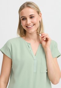 Kurzärmlige, hellgrüne Bluse aus weichem Stoff, mit einem V-Ausschnitt, Brusttasche und unaufdringlichem Kragendesign.