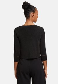 Fekete, rövid, kötött pulóver háromnegyedes ujjal és kis lyukasztott részletekkel az ujj végein, sima textúrával és fénylő hatással.