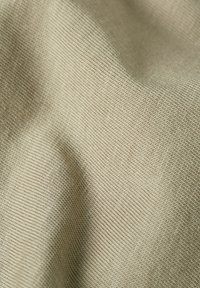 Lichtbeige stof met een fijne, gestructureerde weving, die zachte plooien en een glad oppervlak toont, wat duidt op een zacht, ademend materiaal.