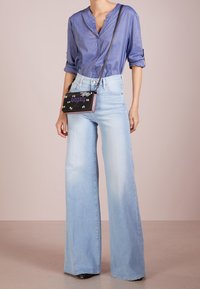 Jeans de pierna ancha de color azul claro con cintura alta, combinados con una camisa abotonada de color azul marino. Un pequeño bolso negro con acentos coloridos completa el look.