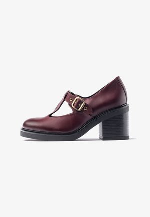 Chaussure à talon en cuir bordeaux avec un design à bride en T, boucle dorée en accent, bout arrondi et talon noir texturé. Style classique et structuré.