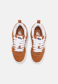Paire de baskets en daim marron avec lacets blancs et semelles blanches, vues de dessus sur un fond uni clair.