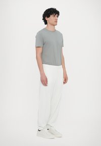 Grå bomulds t-shirt kombineret med hvide, bløde bukser med elastisk talje og hvide sneakers. Enkelt design uden mønstre eller markante detaljer.